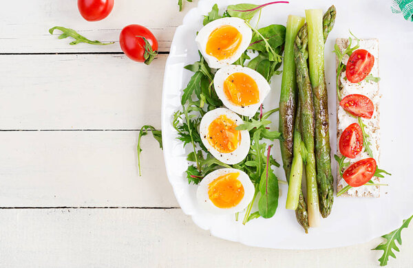Green asparagus with boiled eggs and sandwich cream cheese on a white plate. Top view, flat lay