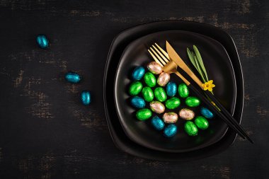 Mutlu Paskalyalar. Paskalya tatili için masa ayarlayın. Paskalya çikolatası yumurtaları ve siyah arka planda çatal bıçak takımı. Üst manzara, düz uzanma