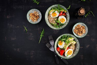 Kahvaltıda haşlanmış yumurta, avokado, domates ve yeşil otlu yulaf lapası. Sağlıklı dengeli yiyecekler. Üst manzara, düz uzanma