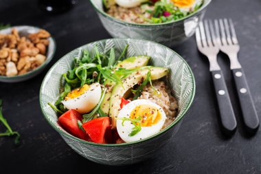 Kahvaltıda haşlanmış yumurta, avokado, domates ve yeşil otlu yulaf lapası. Sağlıklı dengeli yiyecekler.