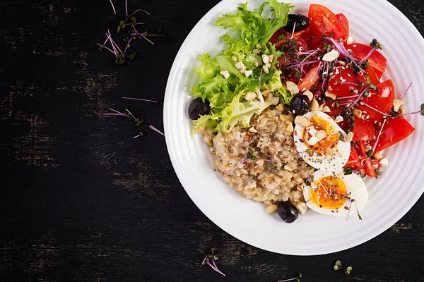 Kahvaltı yulaf lapası haşlanmış yumurta, vişneli domates, zeytin, fındık ve mikroyeşillik. Sağlıklı dengeli yiyecekler. Üst görünüm, genel görünüm
