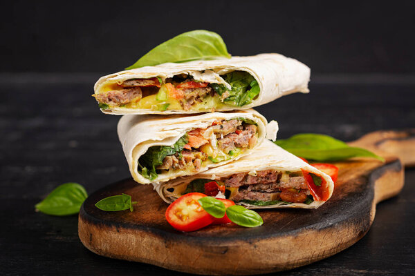 Grilled tortilla wraps with beef and fresh vegetables on wooden board. Beef burrito. Mexican food. Healthy food concept.