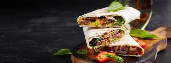 Grilled tortilla wraps with beef and fresh vegetables on wooden board. Beef burrito. Mexican food. Healthy food concept. Banner