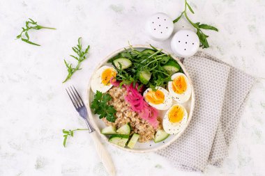 Kahvaltı yulaf lapası haşlanmış yumurta, salatalık, kırmızı soğan ve yeşillik. Sağlıklı dengeli yiyecekler. Üst görünüm