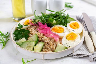 Kahvaltı yulaf lapası haşlanmış yumurta, salatalık, kırmızı soğan ve yeşillik. Sağlıklı dengeli yiyecekler.