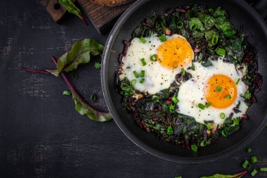 Kahvaltıda. Yeşil pancar yapraklı kızarmış yumurta, sarımsak, biber ve tavada yeşil soğan. Üst manzara, düz uzanma