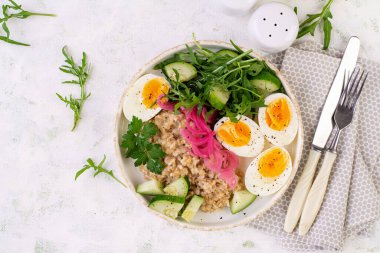 Kahvaltı yulaf lapası haşlanmış yumurta, salatalık, kırmızı soğan ve yeşillik. Sağlıklı dengeli yiyecekler. Üst görünüm