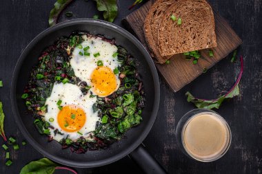 Kahvaltıda. Yeşil pancar yapraklı kızarmış yumurta, sarımsak, biber ve tavada yeşil soğan. Üst manzara, düz uzanma