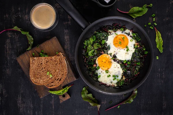 Kahvaltıda. Yeşil pancar yapraklı kızarmış yumurta, sarımsak, biber ve tavada yeşil soğan. Üst manzara, düz uzanma