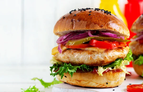 Chicken hamburger. Sandwich with chicken burger, tomatoes, cheese, pickled cucumber and lettuce. Cheeseburger.
