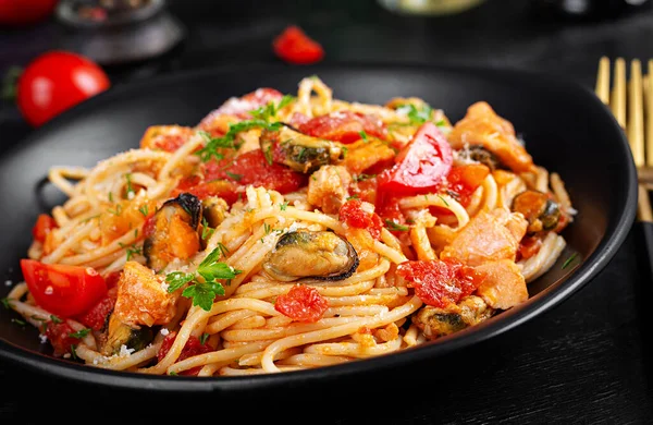 Classic italian pasta spaghetti marinara with mussels and salmon on dark table. Spaghetti pasta with sauce marinara.