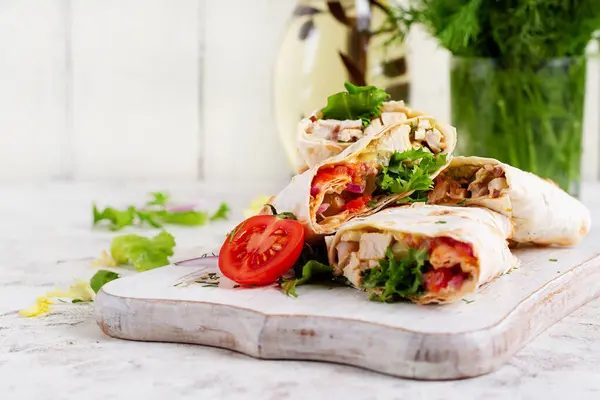 Grilled tortilla wraps with chicken and fresh vegetables on white wooden board. Chicken burrito. Mexican food. Healthy food concept.