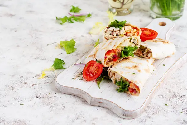 Grilled tortilla wraps with chicken and fresh vegetables on white wooden board. Chicken burrito. Mexican food. Healthy food concept.