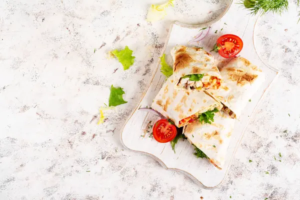 Grilled tortilla wraps with chicken and fresh vegetables on white wooden board. Chicken burrito. Mexican food. Healthy food concept. Top view
