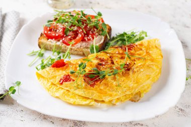 Peynirli omlet ve beyaz tabakta domatesli tost. Frittata - İtalyan omleti.