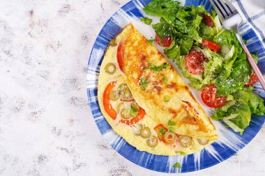 Domatesli omlet, yeşil zeytin ve mavi tabakta taze salata. Frittata - İtalyan omleti. Üst manzara, düz uzanma