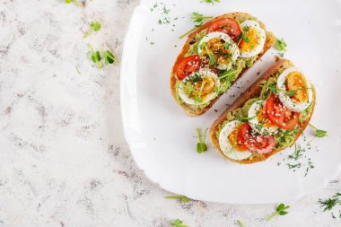 Avokado, haşlanmış yumurta, domates ve beyaz tabakta mikroyeşil ile nefis bir tost. Sağlıklı beslenme, kahvaltı. Keto diyet yemeği. Moda yemekler. Üst görünüm