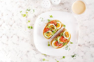 Avokado, haşlanmış yumurta, domates ve beyaz tabakta mikroyeşil ile nefis bir tost. Sağlıklı beslenme, kahvaltı. Keto diyet yemeği. Moda yemekler. Üst görünüm