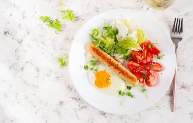Keto kahvaltısı. Kızarmış yumurta, tavuk sosisi ve taze salata. Üst manzara, düz uzanma