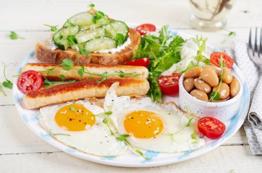 İngiliz kahvaltısı. Keto kahvaltısı. Kızarmış yumurta, fasulye, tavuk sosisi ve kahve fincanı..