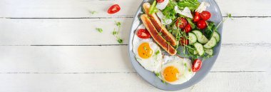 Keto kahvaltısı. Kızarmış yumurta, tavuk sosisi ve taze salata. Üst görünüm, afiş