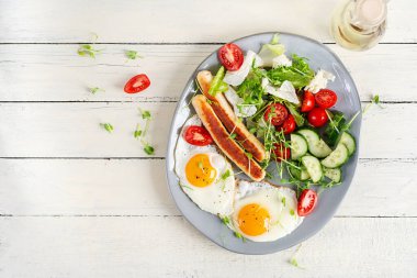 Keto kahvaltısı. Kızarmış yumurta, tavuk sosisi ve taze salata. Üst manzara, düz uzanma