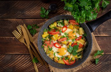 Fried eggs and potatoes, tomatoes, zucchini  and chili peppers on wooden table.  Top view