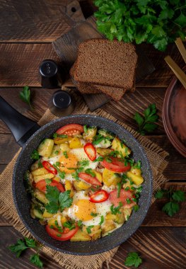 Fried eggs and potatoes, tomatoes, zucchini  and chili peppers in a rustic style.  Overhead