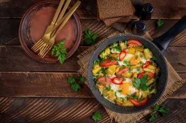 Fried eggs and potatoes, tomatoes, zucchini  and chili peppers in a rustic style.  Top view