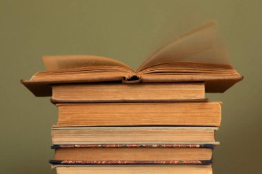 Diğer eski kitapların üzerinde açık bir kitap yığını. Sayfaların hareketleriyle hareket eden bir kitabın sayfaları. Yeşil zeytin arkaplanı üzerine eski kitaplar.
