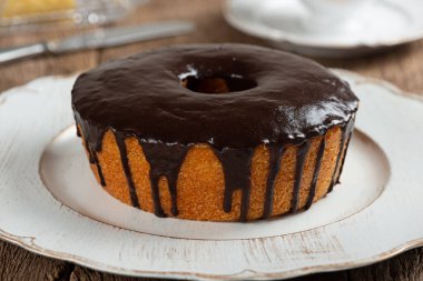 Homemade round carrot cake with chocolate coating, typical Brazilian food at a June party and a plate on a rustic wooden table.