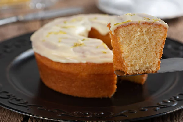 Homemade round lemon cake with topping and lemon zest on a plate, typical Brazilian food at a June festival and dish on a rustic wooden table with selective focus on the slice on the spatula.