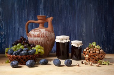 Hayat, seramik sürahi, kavanozda reçel, fındık ve ahşap bir masada çeşitli meyveler.