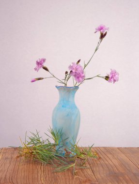 Durgun hayat, seramik vazo, ahşap bir masada karanfil.