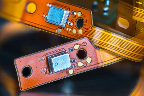 Beautiful flex electronic printed circuits on yellow and orange colored strips on a black blurry background. Closeup of bendy PCB or small components on flexible ribbon cables from inside of headphones.