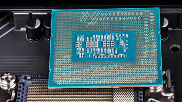 Closeup of processor installation to computer mainboard socket. Green printed circuit board with surface-mount assembly of small electronic components on bottom side of modern central processing unit.