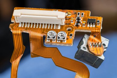 Turuncu baskılı devre kartı, esnek kurdele kabloları, küçük elektronik parçaları ve beyaz konnektörü var. Dijital CD / DVD optik disk sürücüsünün içinden düz ve esnek PCB 'ye yakın çekim. E-atık yok etme.