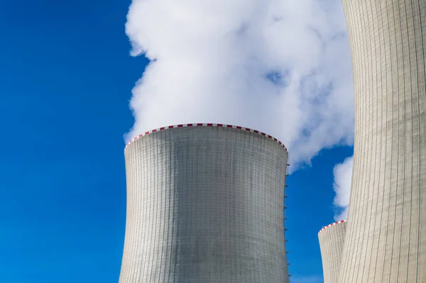 Closeup of cooling towers power station with white clouds of steam on a blue sky background. Large chimneys details for remove waste heat by water evaporation in nuclear generating plant. Energy crisis.