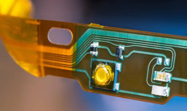 Plastic strip with flexible printed circuit and electronic surface mounted components. Closeup of bent ribbon cable with green and yellow lines of flat PCB dismantled from headphones. E-waste recycle. clipart