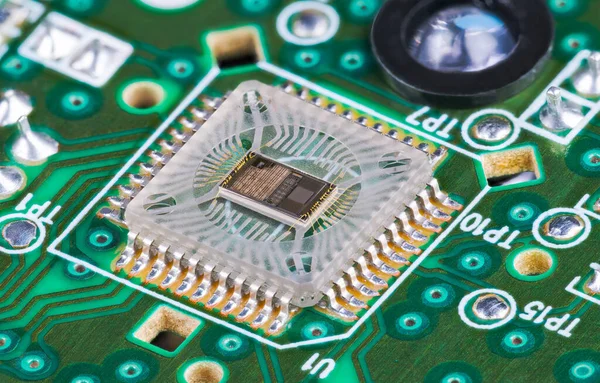 Closeup of microchip die inside optical sensor on green printed circuit board. Electronic square transparent surface mounted component to detect motion and round light source on PCB in computer mouse.