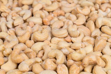 Mutfak arka planında nefis tuzlu kaju fıstığı yakın plan. Anacardium oksidentale. Açık kahverengi böbrek şeklinde kavrulmuş kaju fıstığı ve beyaz tuz kristalleri. Yenilebilir tohumlardan bej dokuda lezzetli yiyecekler..