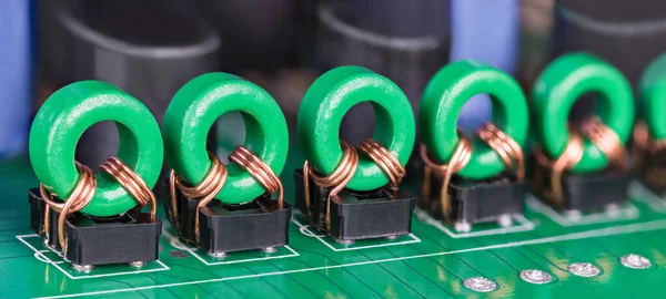 Row of toroidal transformer inductors on PCB for audio or video signal galvanic isolation. Closeup of electronic coils with copper wire on green ferrite core in black holders on printed circuit board.