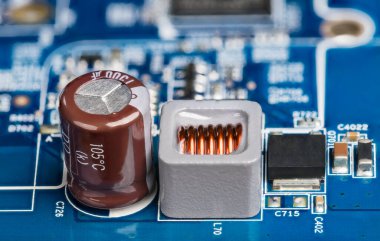 Bulanık PCB arka planında indüktör, elektrolitik kapasitör ya da transistör kapalı. Mavi güç kaynağı, yüzeye bağlı elektronik bileşenler ve kahverengi yoğunlaştırıcı veya gri bobin içeren devre kartı.