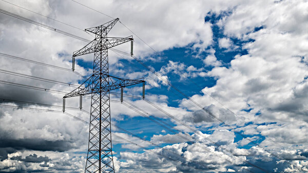 Transmission tower top part silhouette on a blue sky background and white clouds. Closeup of electricity pylon truss structure and high-voltage cables. Overhead power line to transmit electrical energy.