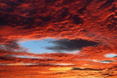 Red cloudscape with blue fallstreak hole in cirrocumulus clouds at evening twilight. Beautiful fiery afterglow on orange sky with unusual cavum at wonder winter sunset. Impressive elliptical skypunch. clipart