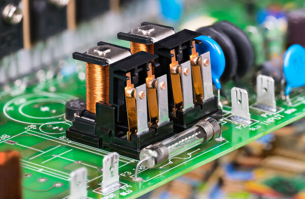 Electronic components as electromagnetic relays or glass electric fuse on green PCB. Closeup two electromechanical switches with copper wire on coil with iron core, yoke and armature on circuit board.