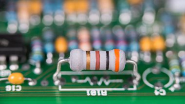 Closeup a white resistor with standard colored code on green printed circuit board. Electronic components with color band system on PCB with beautiful bokeh in blur background. Electrical engineering. clipart