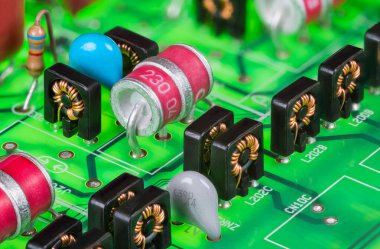 Red electrode gas discharge surge arresters and toroid inductors in black case. Closeup of electronic components on green printed circuit board in digital telephone switch analog part line protection. clipart