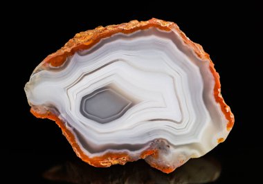 Siyah bir arka planda cilalanmış değerli bir taş var. Gemstone kesiti pürüzsüz yüzey, beyaz gri çizgili desen ve kalın paslı turuncu kenar. Fas kökenli doğal mineral.