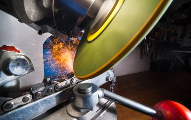 Elektrikli testerenin yaklaşması öğütücü makinesinin dönen diski ile keskinleştiriliyor. Sivri uçlu jant, sivri uçlu kıvılcımlar. Profesyonel elektrikli bileyicinin kesme aletinin çelik dişlerini gıcırdatıyor..